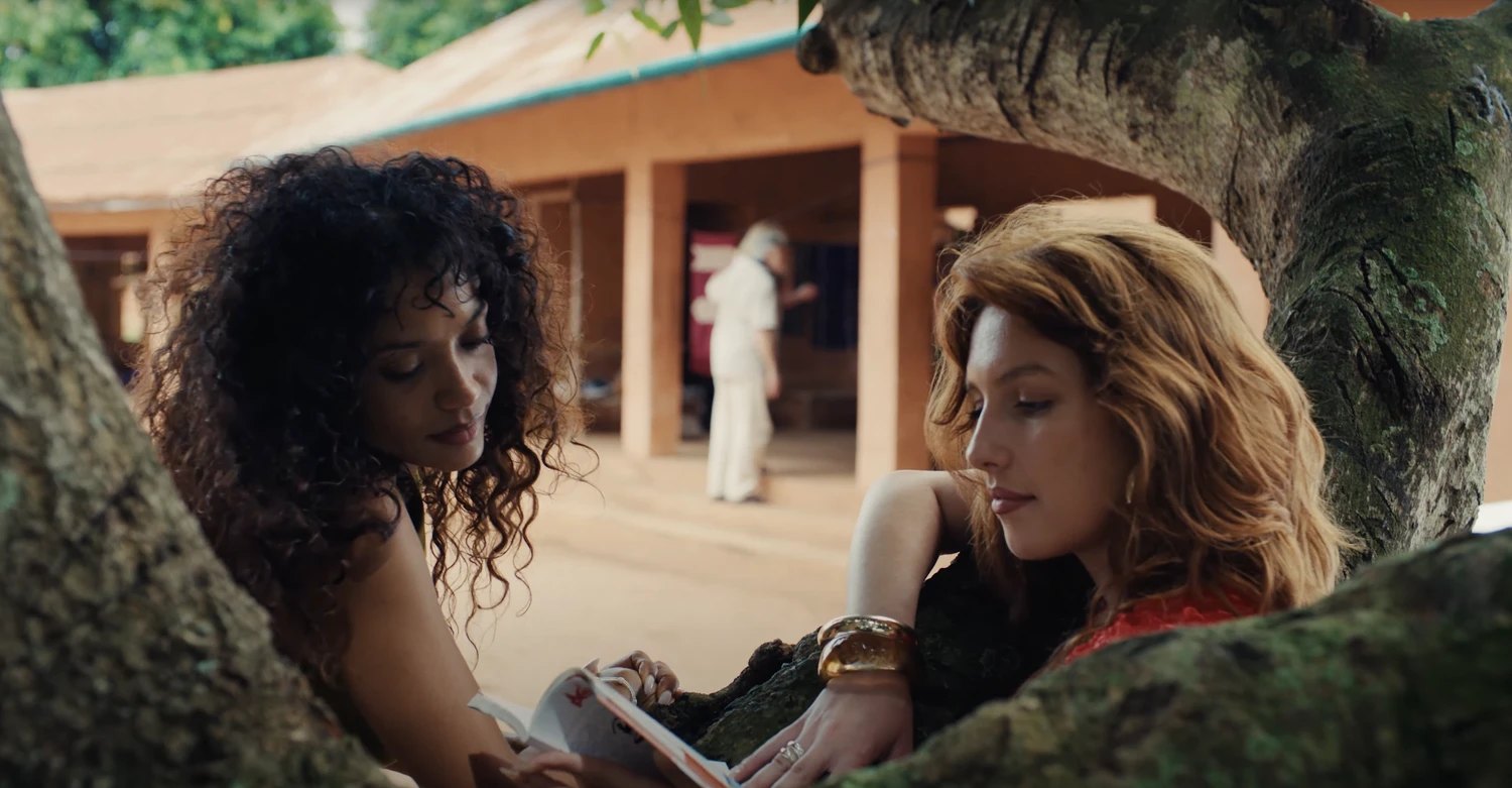 Two guests reading under a tree in the red-earth courtyard